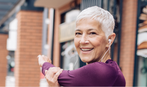 An elder woman stretching before a run wearing ear buds.